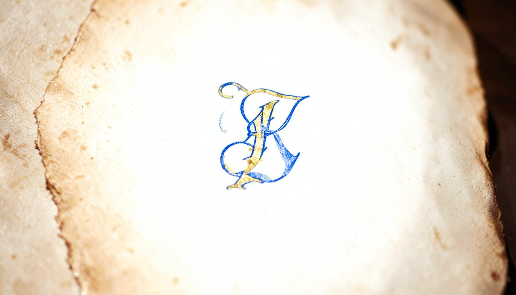 Stimmungsvolle Aufnahme einer mittelalterlichen Handschrift mit goldener Initiale auf Pergament, warme Braun- und Goldtöne